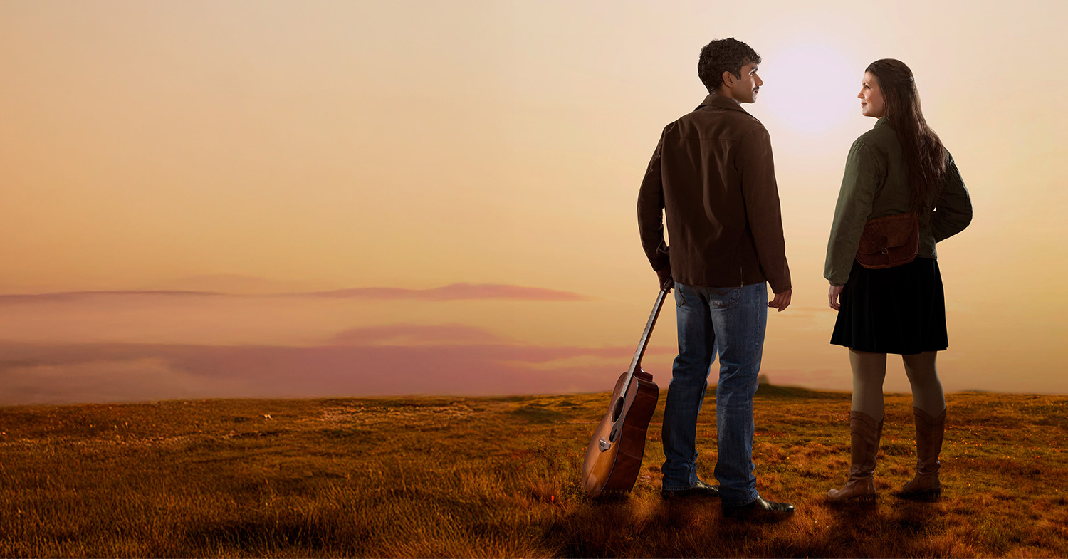 Två ungdomar vid ett öde landskap. Pojken har en gitarr